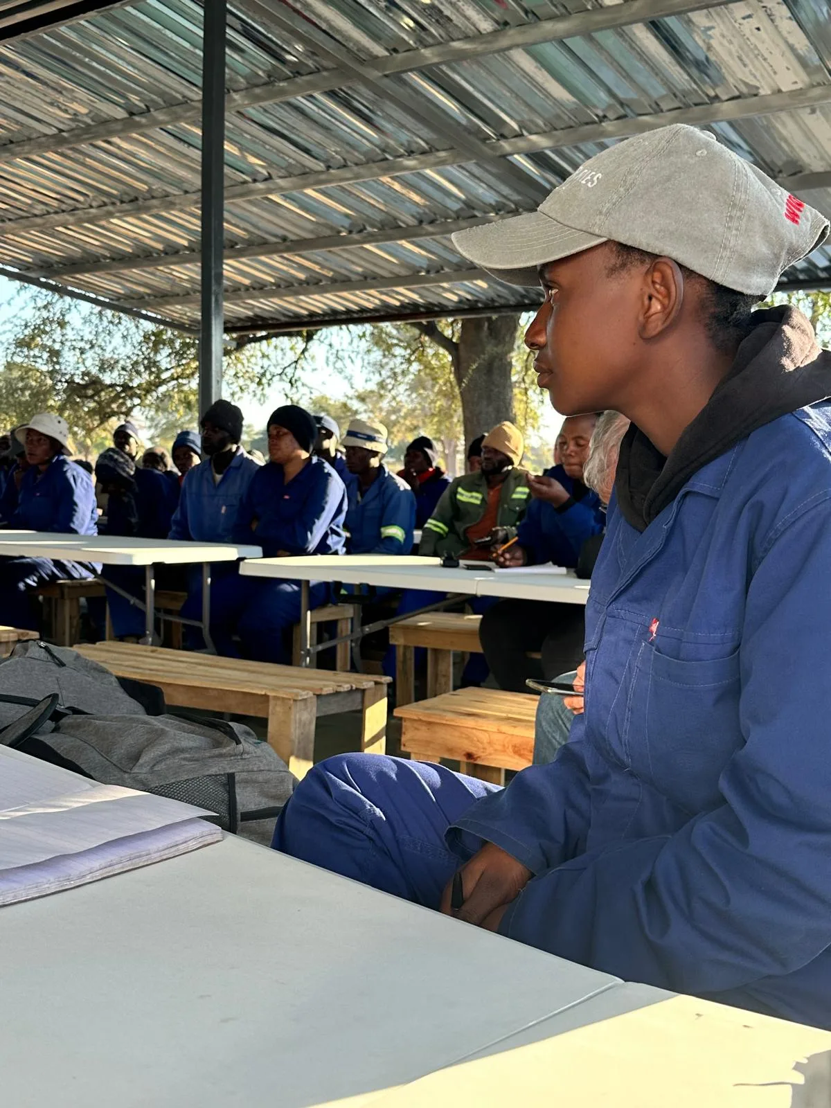 Farm workers in blue overalls at a training session under a shade roof