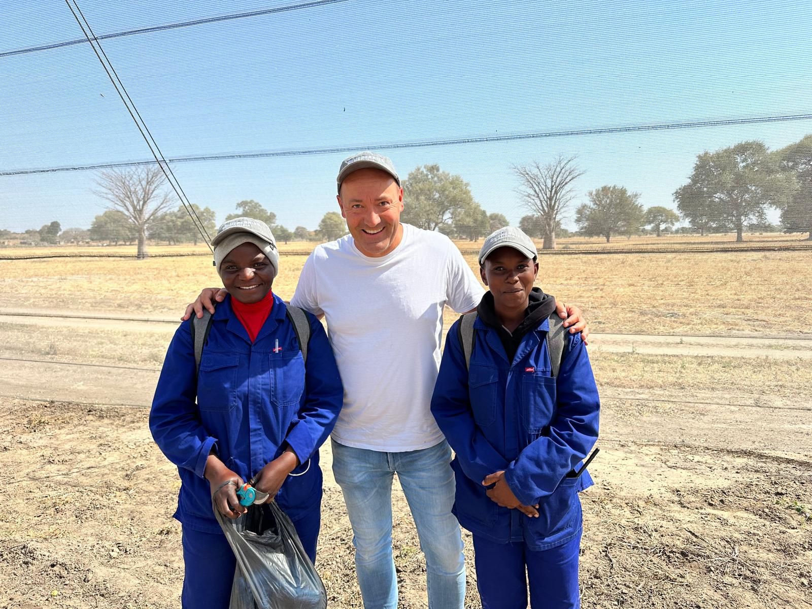 Two farm workers in blue overalls with a colleague in the field