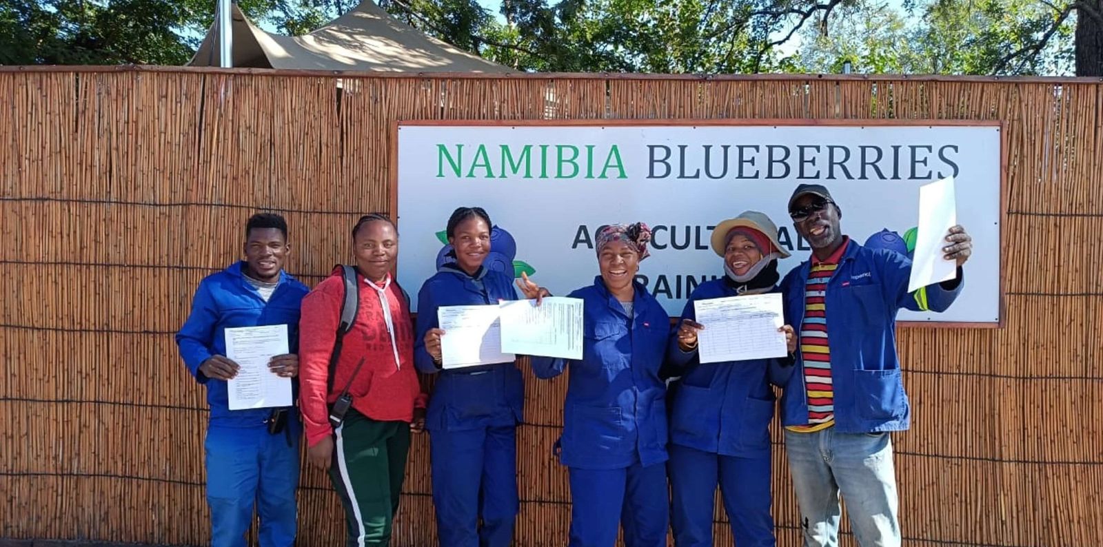 Trainees holding their certificates in front of the Namibia Blueberries agricultural training sign